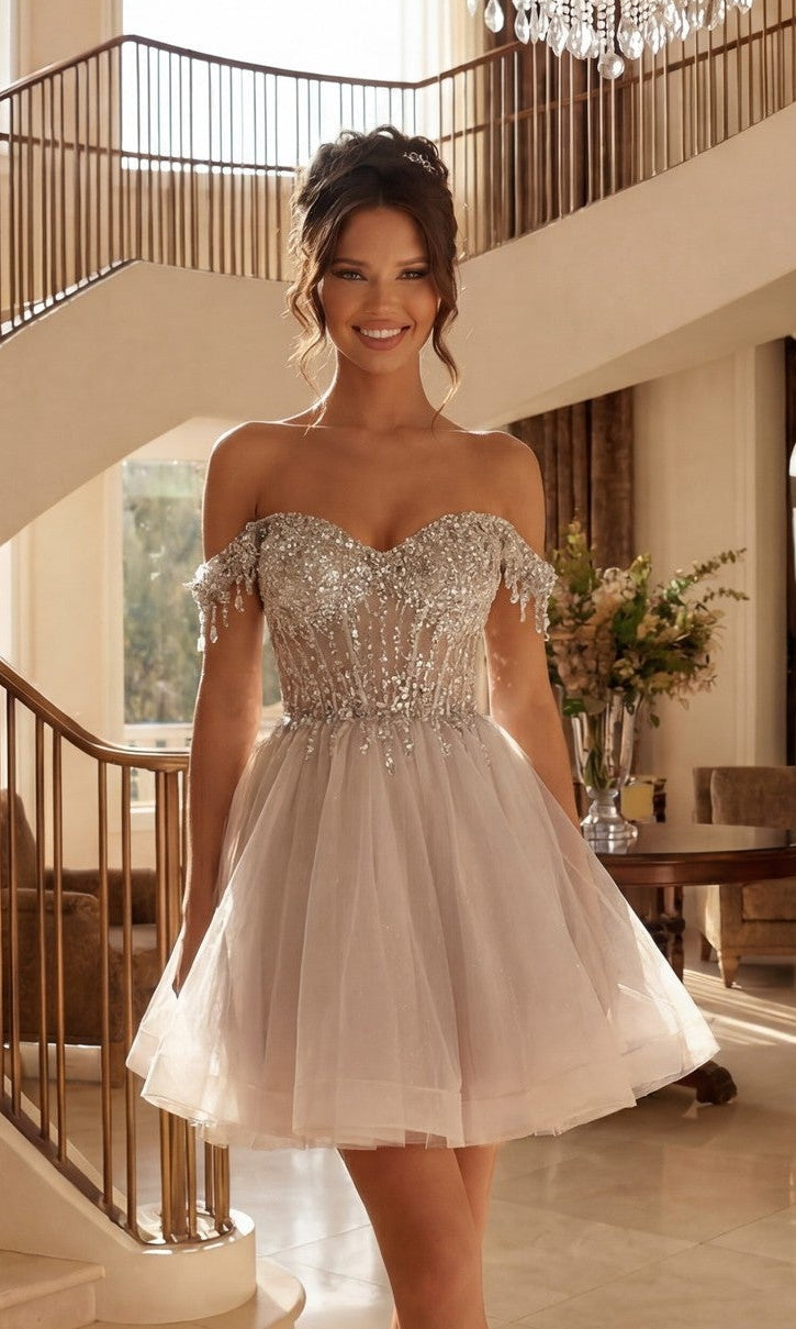 A woman in the Juliet JT947L Short Champagne Corset Prom Dress in silver smiles while standing in a spacious, elegant room with a staircase and large windows.